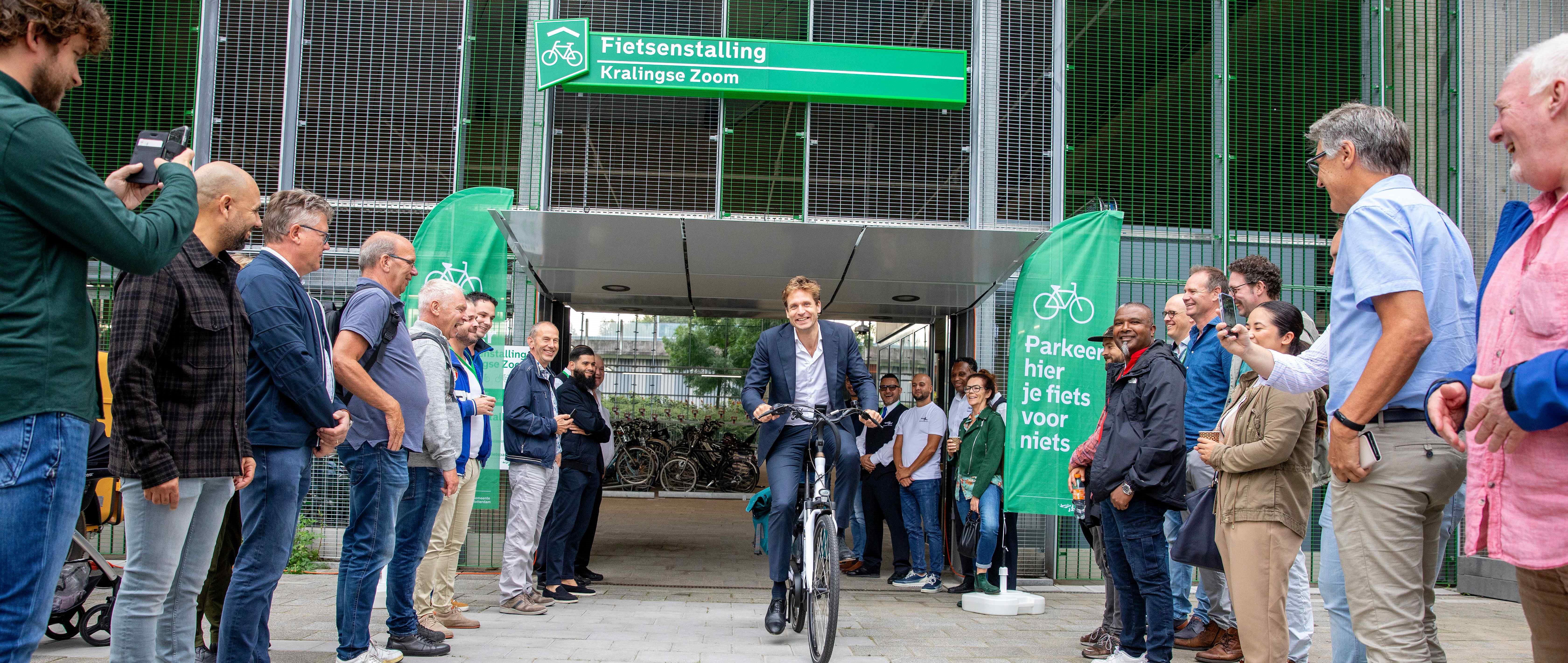 Wethouder Vincent Karremans komt uit de fietsenstalling Kralingse Zoom fietsen ter gelegenheid van de opening. Mensen kijken toe.