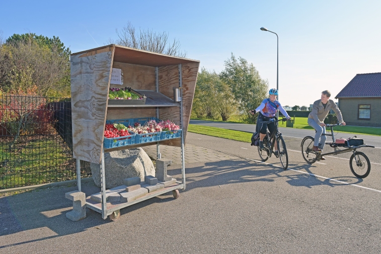 Fietsburgemeesters Marja van der Ende en Marcel Kleizen fietsen langs een groentestalletje