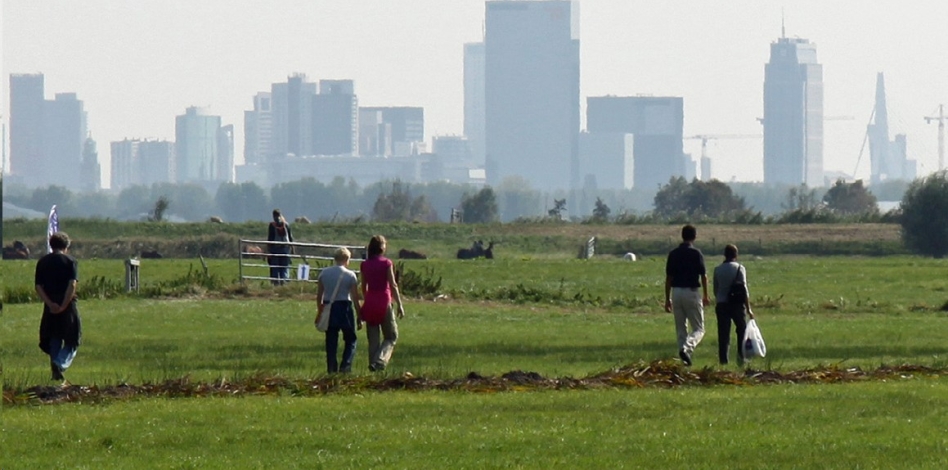 Mensen wandelen door de weilanden. Op de achtergrond skyline van Rotterdam.