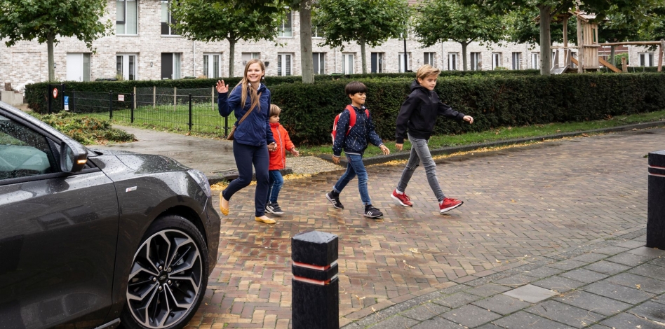 Een auto stopt voor een moeder met drie overstekende kinderen op weg naar school.