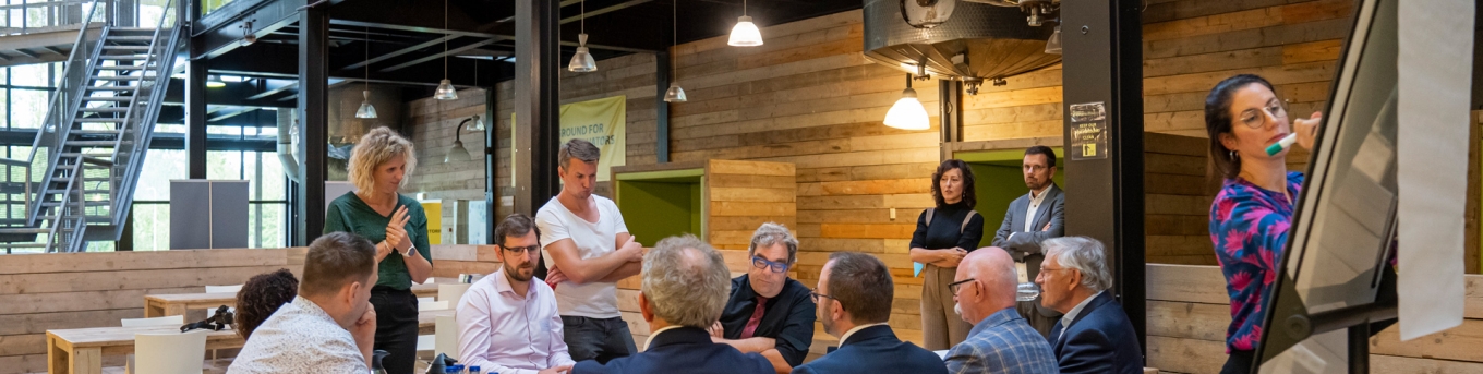 Mensen rondom een tafel zijn in gesprek over de Strategische Agenda MRDH. Iemand schrijft wat op het bord.