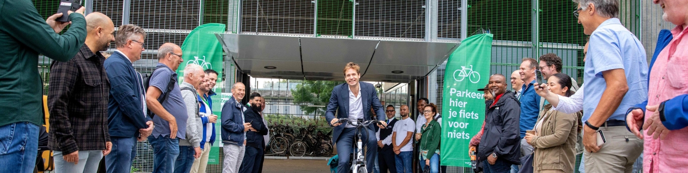 Wethouder Vincent Karremans komt uit de fietsenstalling Kralingse Zoom fietsen ter gelegenheid van de opening. Mensen kijken toe.