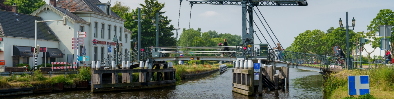 De Nieuwe Tolbrug gezien vanaf het water, fietsers gaan lopend met de fiets aan de hand over de brug.
