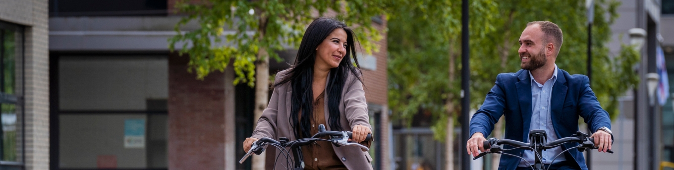 Vrouw en man rijden naast elkaar op de fiets langs kantoren