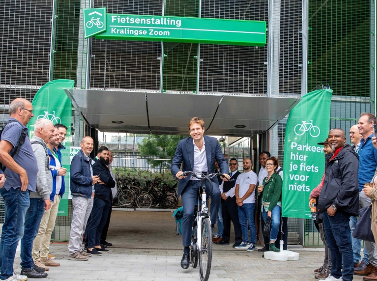 Wethouder Vincent Karremans komt uit de fietsenstalling Kralingse Zoom fietsen ter gelegenheid van de opening. Mensen kijken toe.