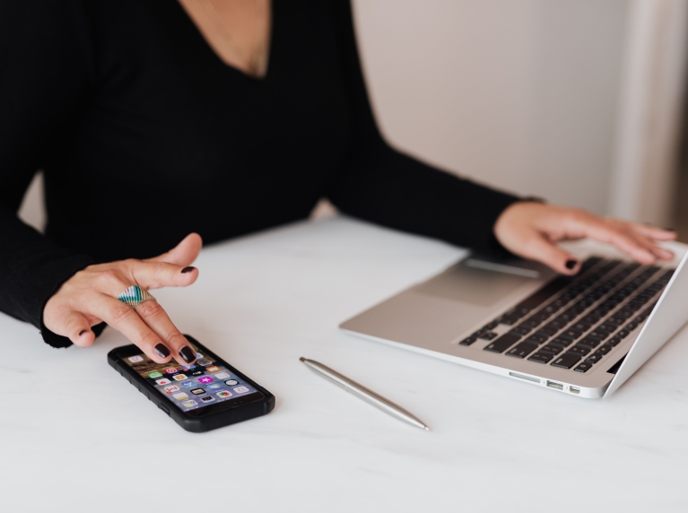 Vrouw achter laptop met telefoon naast zich