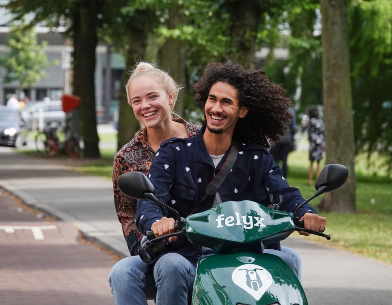 Jongen rijdt op deelscooter met meisje achterop