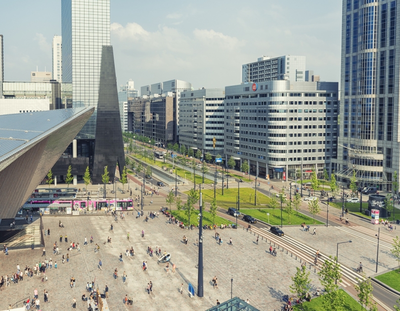 Station Rotterdam Centraal en de omgeving van bovenaf gefotografeerd. Op de foto zijn reizigers, de tram, auto's en de hoge gebouwen te zien.